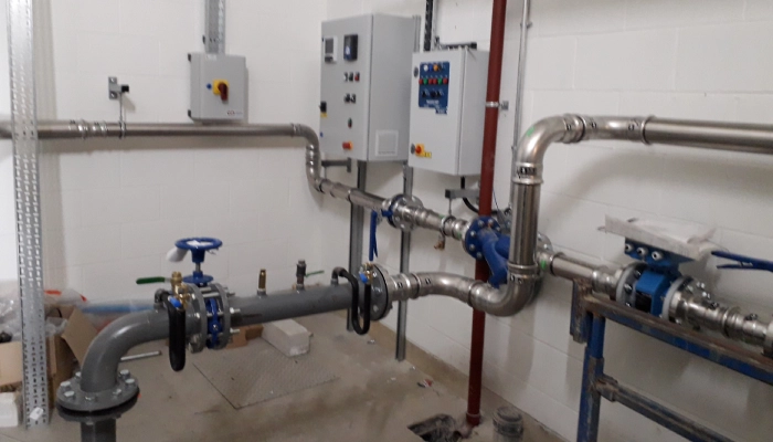 WJ UK services: Internal view of a mechanical room featuring stainless steel pipework, valves, and control panels linked to the buildings management system (BMS) for a ground source energy open loop system installation by WJ UK.