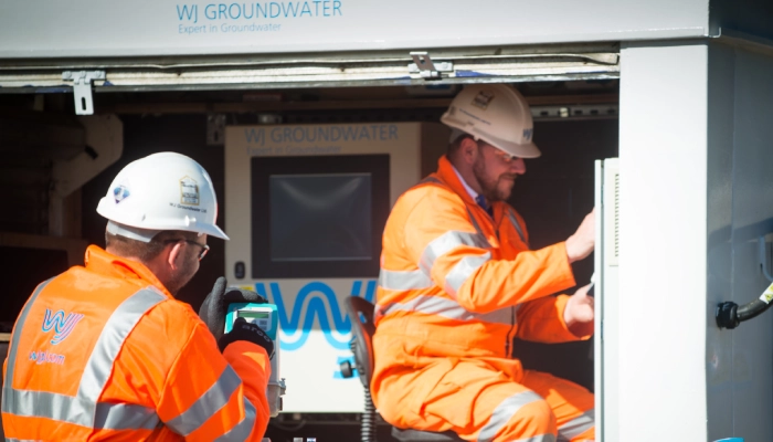 WJ UK technicians conducting a pumping test using flow meters and automated control cabin to monitor groundwater levels and discharge flows in real time, as per our services.