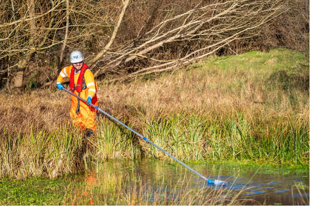 Person wading through water, collecting samples. Sizewell C| Hydrogeological Services